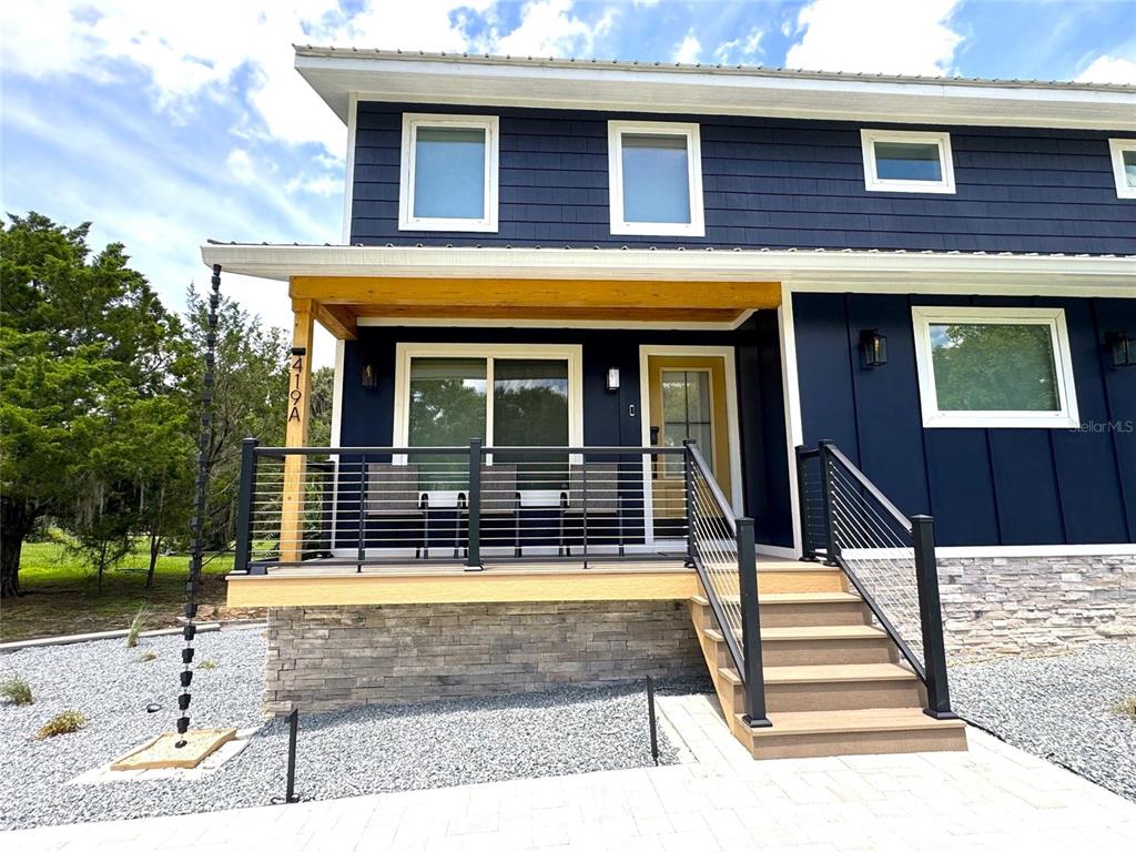 A two-story blue house features a covered front porch with metal railings and stone siding — 419 N APOPKA AVENUE, INVERNESS, FL