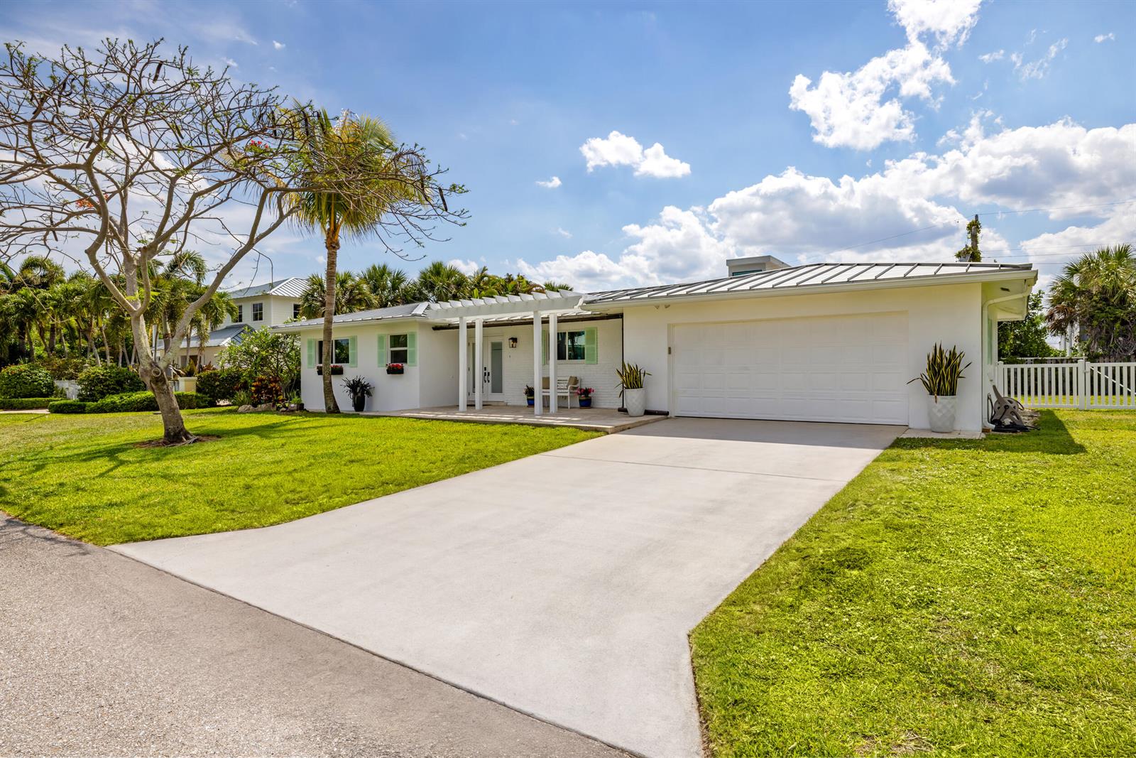 A white single-story house features a concrete driveway, a pergola-covered entrance, and a metal roof — 461 Apollo Drive, Juno Beach FL 33408, JUNO BEACH, FL