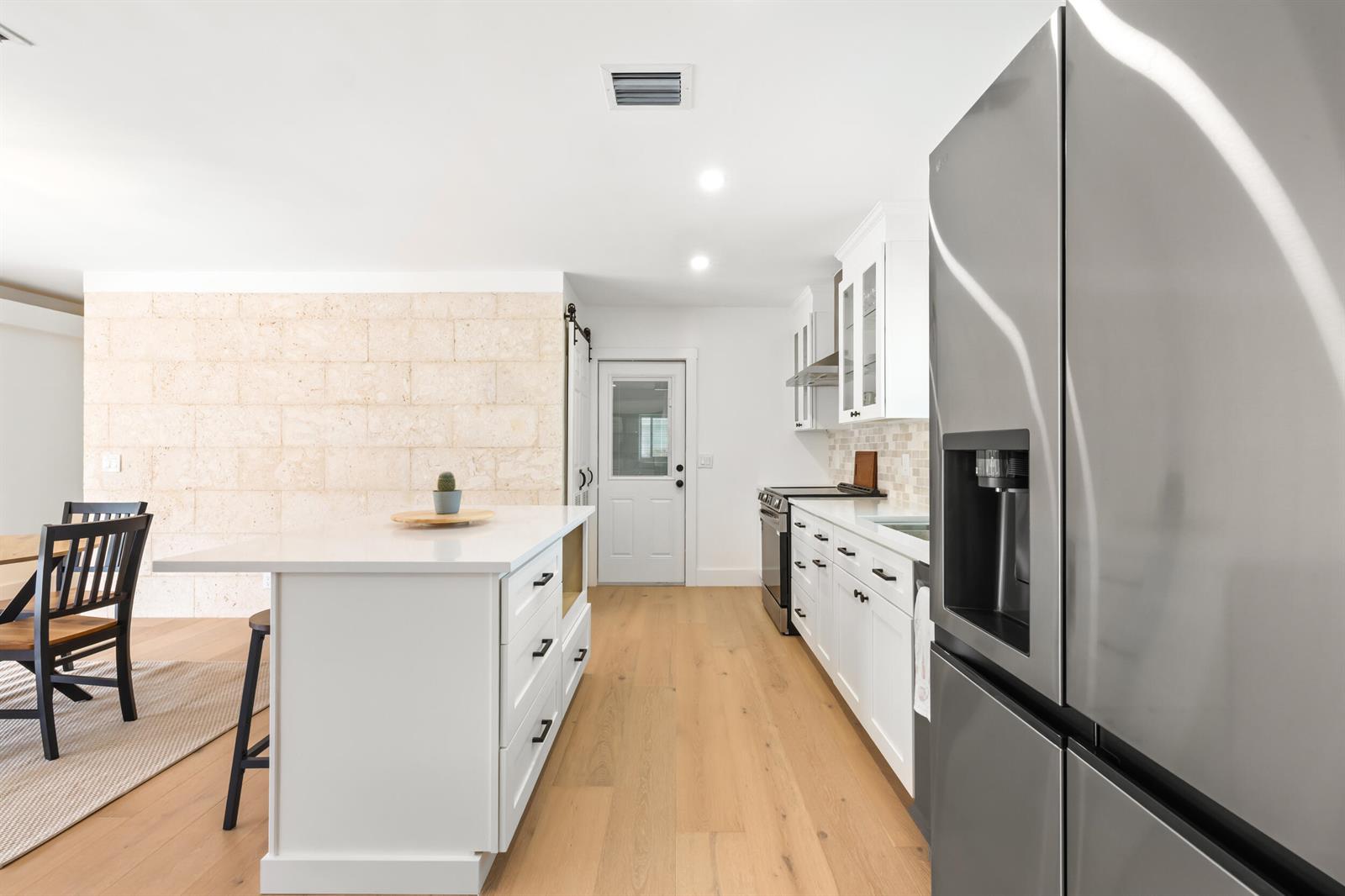A kitchen features white cabinetry, a central island, stainless steel appliances, and a stone accent wall — 461 Apollo Drive, Juno Beach FL 33408, JUNO BEACH, FL