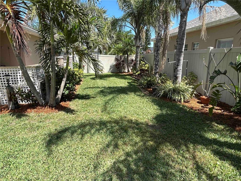 A grassy backyard features palm trees, landscaping beds, and a white vinyl privacy fence — 443 YORK DALE DRIVE, RUSKIN, FL