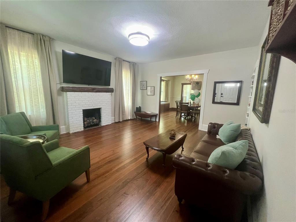 A living room features a white brick fireplace, hardwood floors, green armchairs, and a sofa — 134 N STONE STREET, DELAND, FL