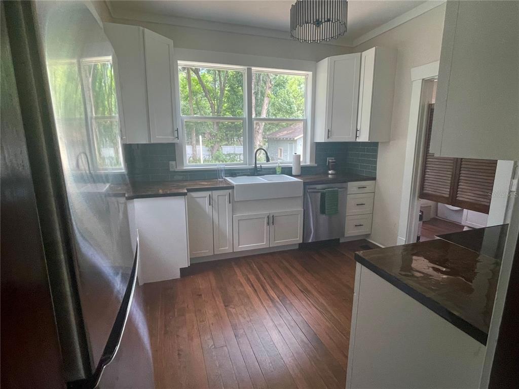 A kitchen features white cabinets, dark countertops, a farmhouse sink, and hardwood flooring — 134 N STONE STREET, DELAND, FL