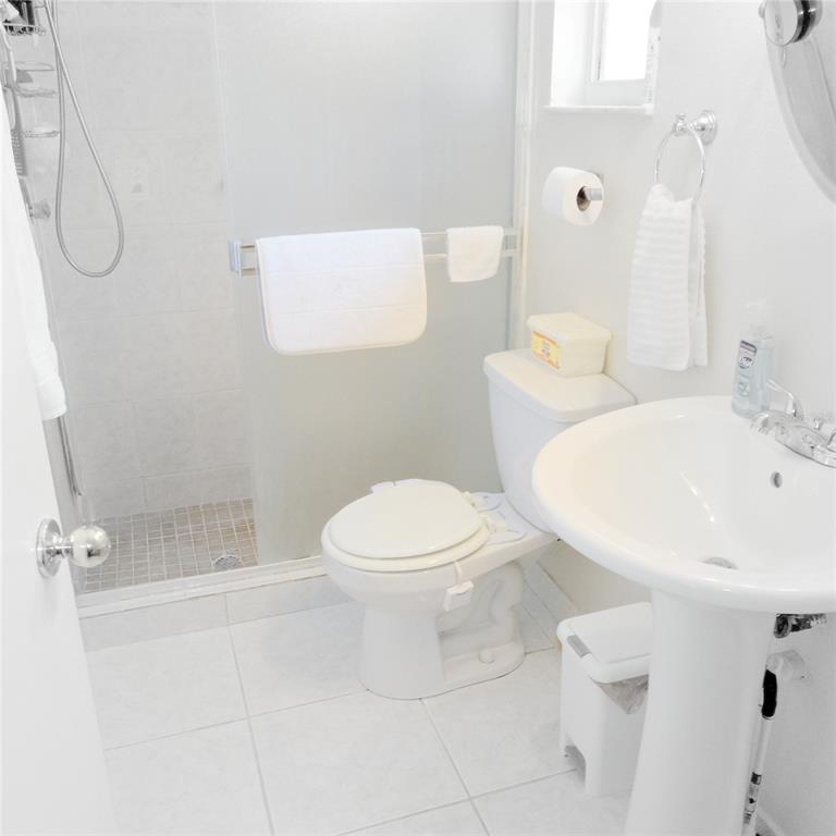 A small, all-white bathroom featuring a pedestal sink, a toilet, and a glass-enclosed shower — 7731 MARIAH COURT, ORLANDO, FL