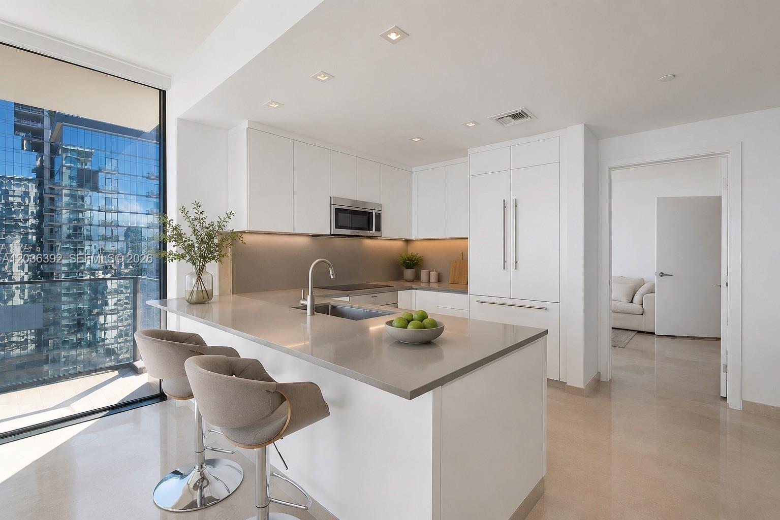 A modern kitchen features white cabinetry, a gray quartz island with bar stools, and floor-to-ceiling windows — 68 SE 6th St # 3301, Miami FL 33131, MIAMI, FL