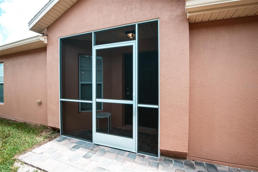 A screened-in entryway with a white door and frame sits on a paved patio — 601 GRAND CANAL DRIVE, KISSIMMEE, FL