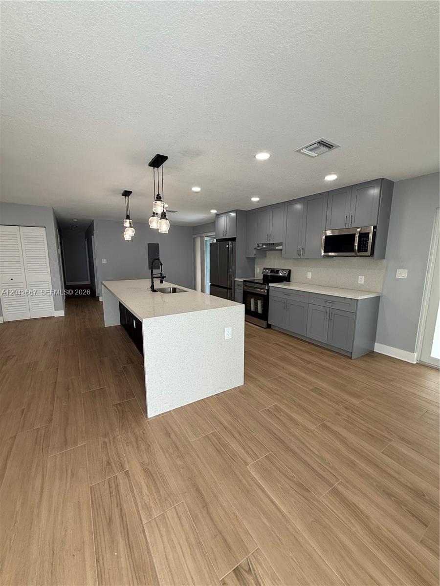 A modern kitchen features gray cabinets, a large quartz island, and light wood-look tile flooring — 311 NW 33rd Ter, Lauderhill FL 33311, LAUDERHILL, FL