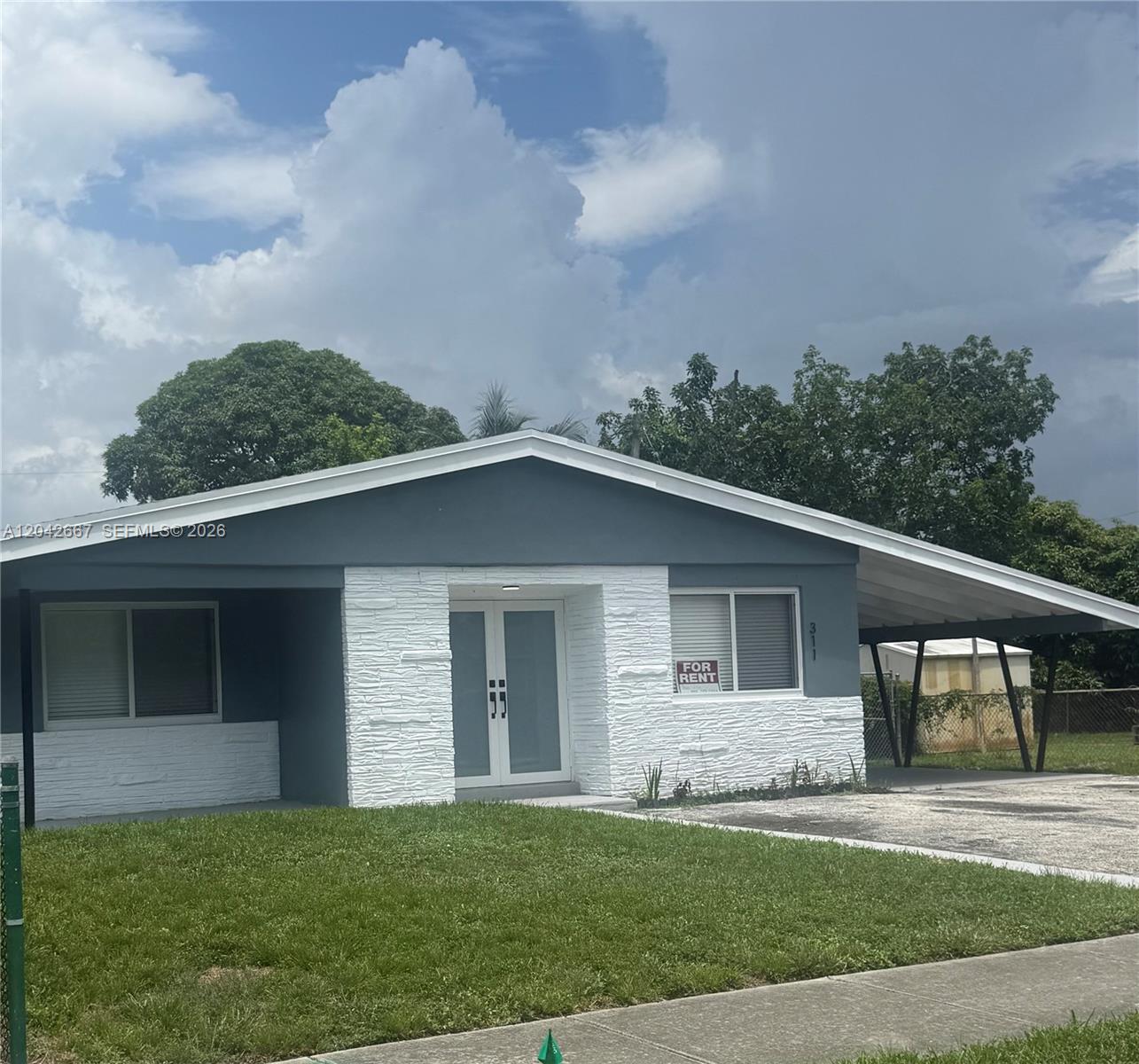 A single-story house features a gray exterior with white stone accents and a side carport — 311 NW 33rd Ter, Lauderhill FL 33311, LAUDERHILL, FL