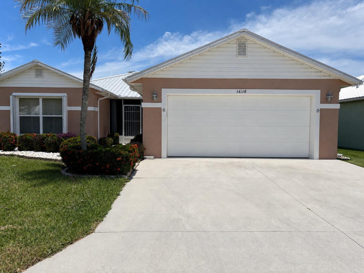 A single-story house with a white garage door, tan stucco walls, and a palm tree — 14168 Cisne Circle, Fort Pierce FL 34951, FORT PIERCE, FL