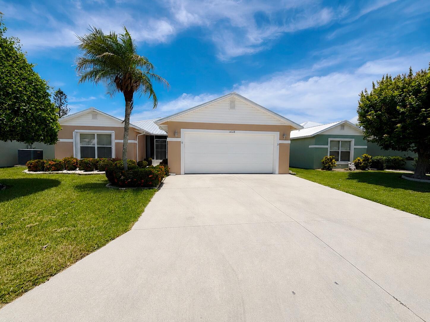 A single-story house with a white garage door, tan siding, and a palm tree out front — 14168 Cisne Circle, Fort Pierce FL 34951, FORT PIERCE, FL