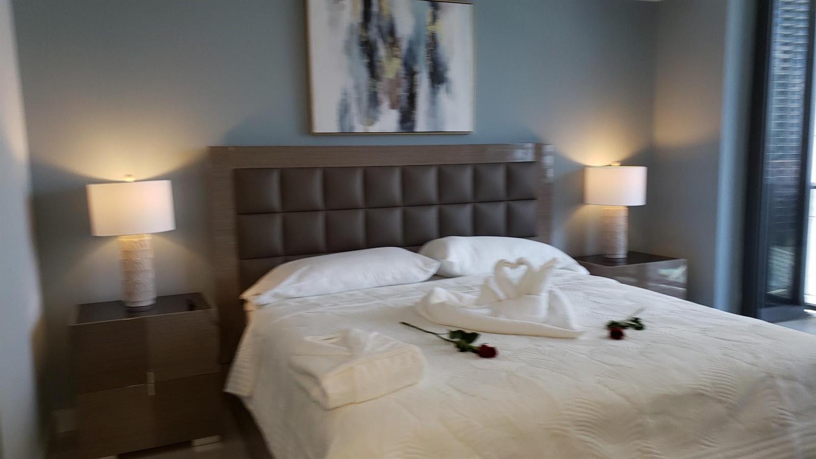 A bedroom features a tufted headboard, two nightstands with lamps, and towel swans on bed — 55 SW 9th Street # 2210, Miami FL 33130, MIAMI, FL
