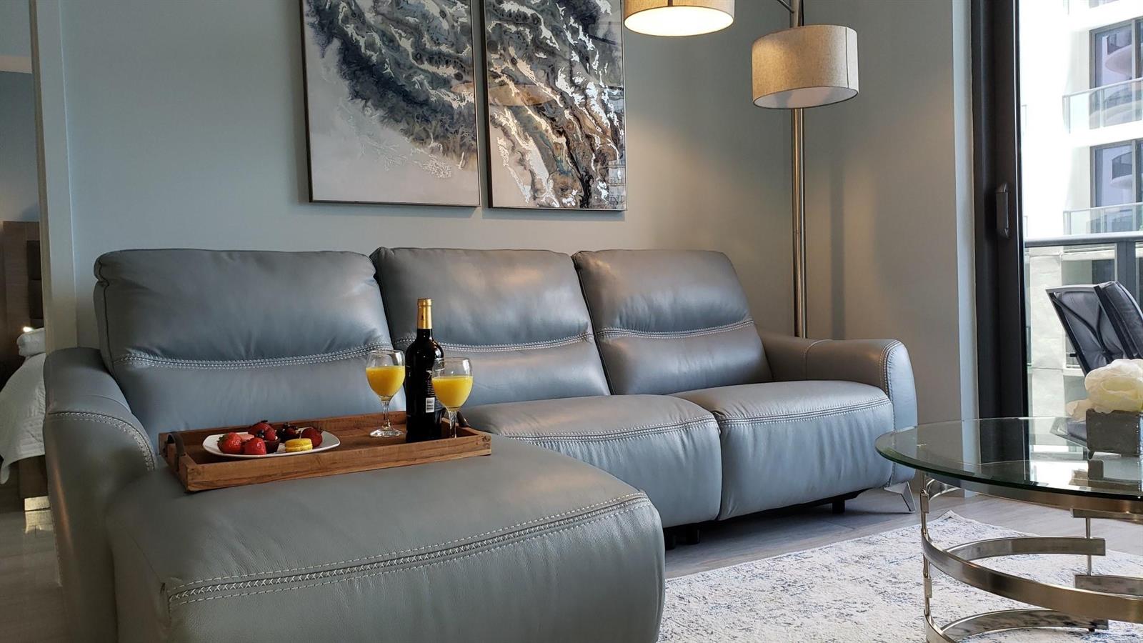 A gray leather sofa with a wooden tray of drinks and fruit sits in a room — 55 SW 9th Street # 2210, Miami FL 33130, MIAMI, FL