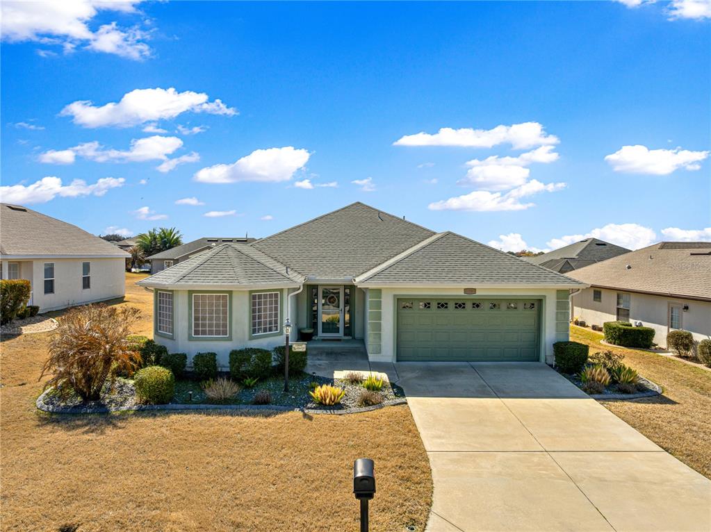 A single-story house with a green garage door and a concrete driveway under a blue sky — 11266 SE 170TH LANE, SUMMERFIELD, FL