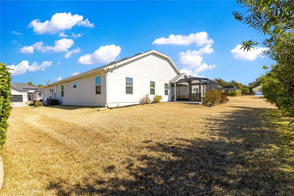 The back exterior of a light-colored house features a screened-in patio and a large yard — 11266 SE 170TH LANE, SUMMERFIELD, FL