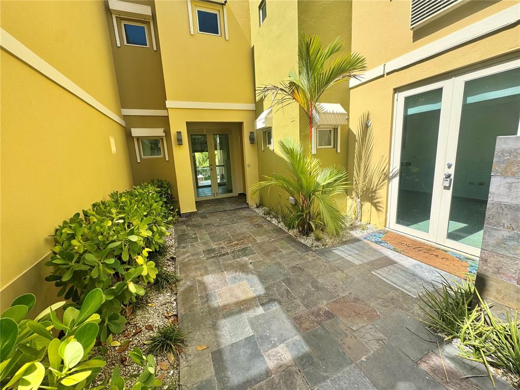 A stone-paved entryway leads to a yellow building with glass doors and tropical plants — 90 CANDELERO DRIVE UNIT 32, HUMACAO, PR