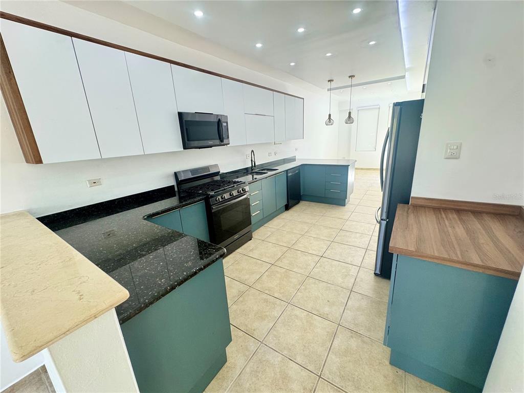 A kitchen features teal lower cabinets, white upper cabinets, black countertops, and tile flooring — 90 CANDELERO DRIVE UNIT 32, HUMACAO, PR