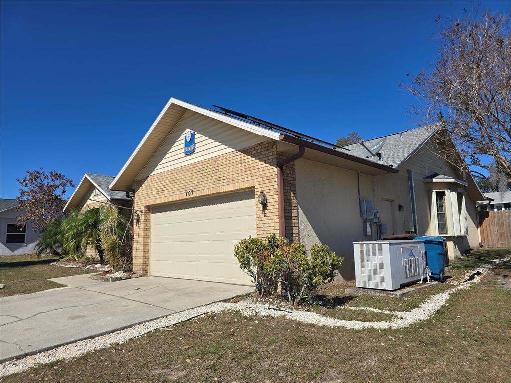 A single-story house with a beige garage, stucco walls, and solar panels on the roof — 707 CAMBRIDGE WAY, LAKE WALES, FL