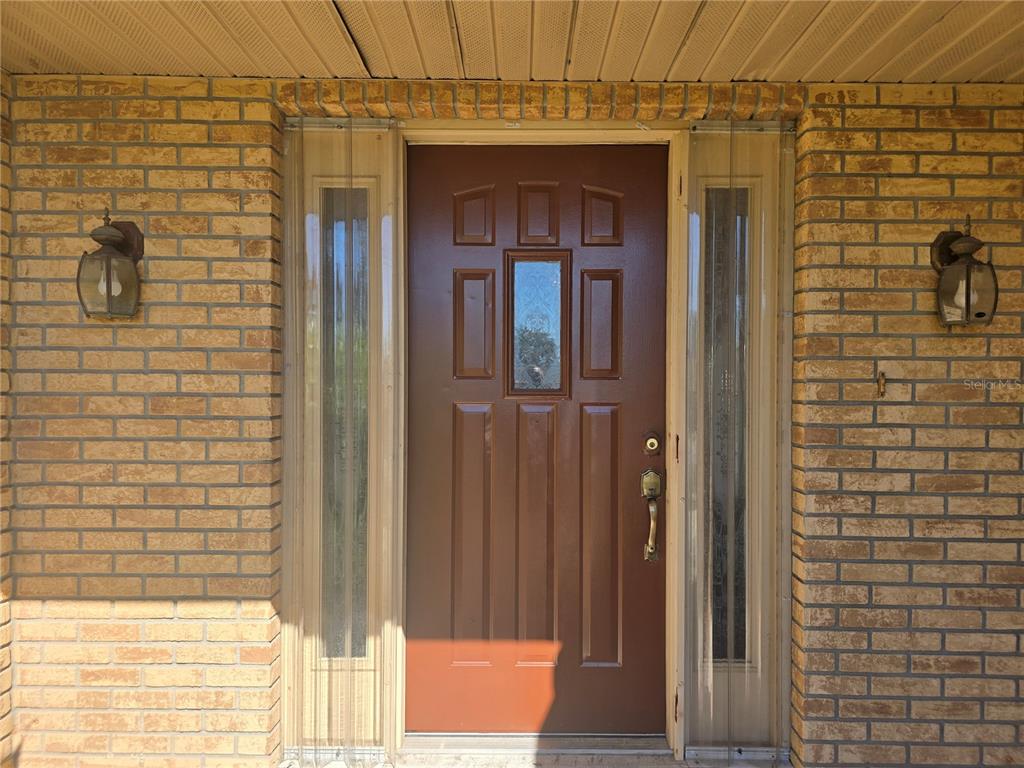 A brown front door with a glass insert is flanked by two vertical sidelight windows — 707 CAMBRIDGE WAY, LAKE WALES, FL