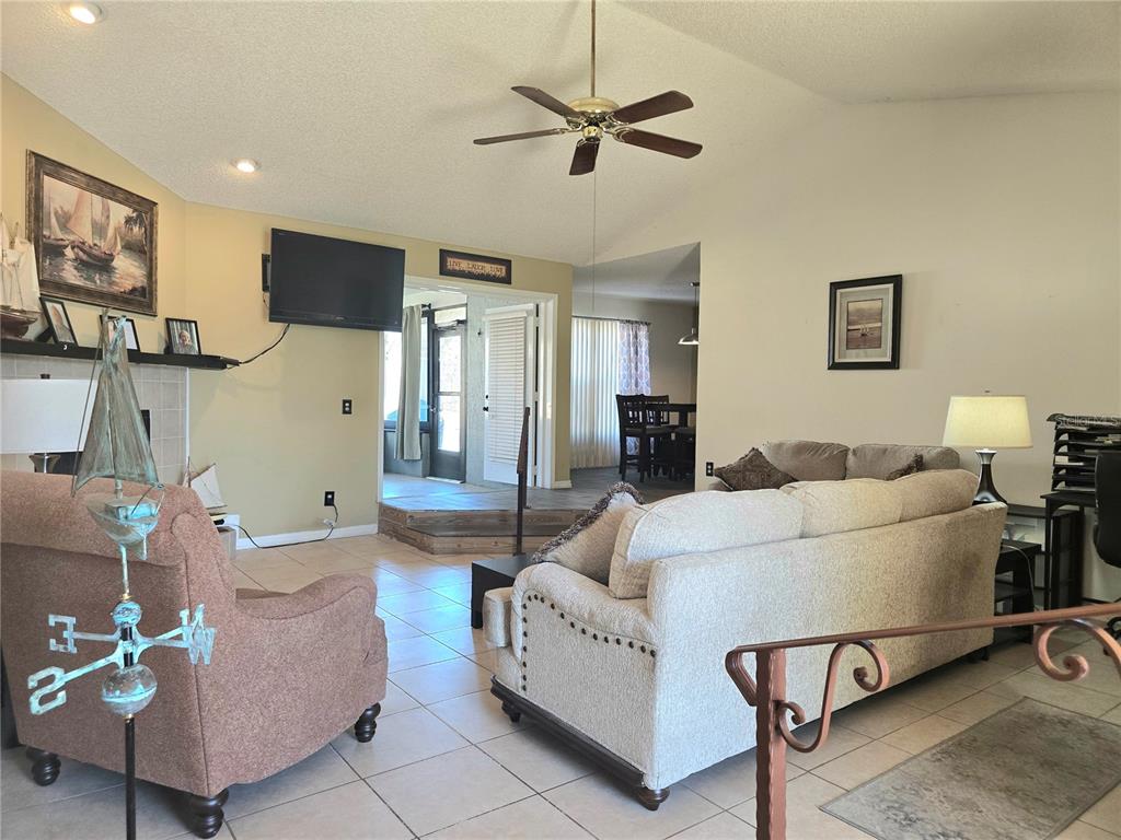 A living room features a vaulted ceiling, tile flooring, a fireplace, and a ceiling fan — 707 CAMBRIDGE WAY, LAKE WALES, FL