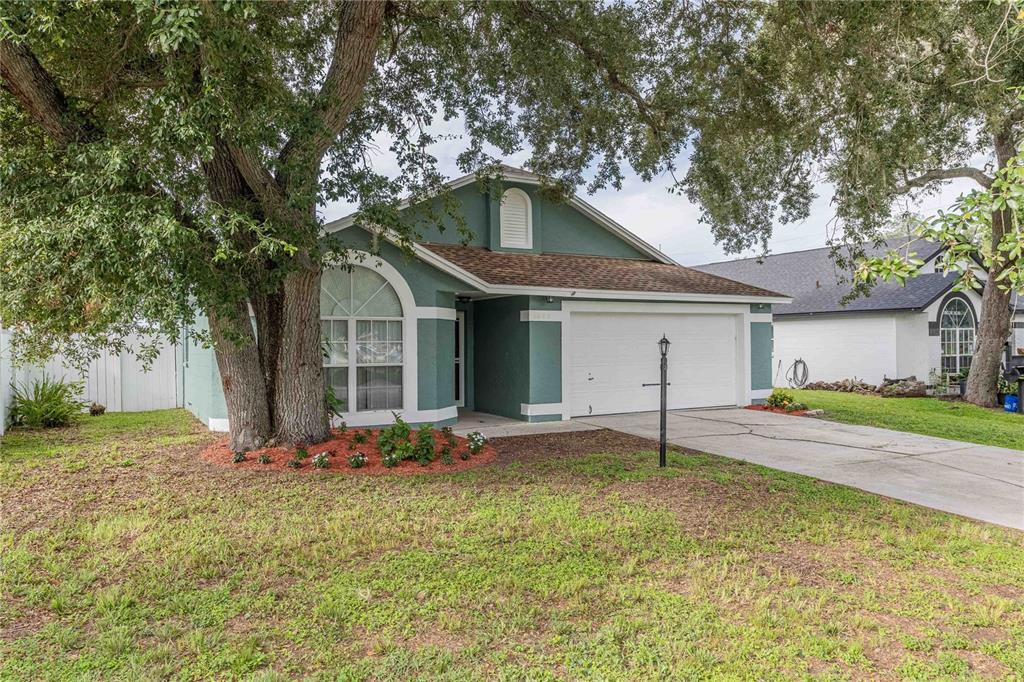 A teal single-story house with a white garage door and a large tree in front — 1695 LAKESIDE DRIVE, BARTOW, FL