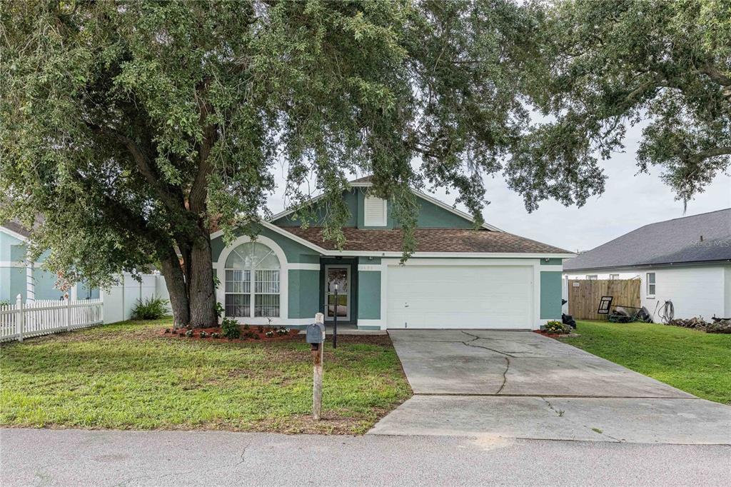 A teal single-story house with a two-car garage and a large tree in the front yard — 1695 LAKESIDE DRIVE, BARTOW, FL