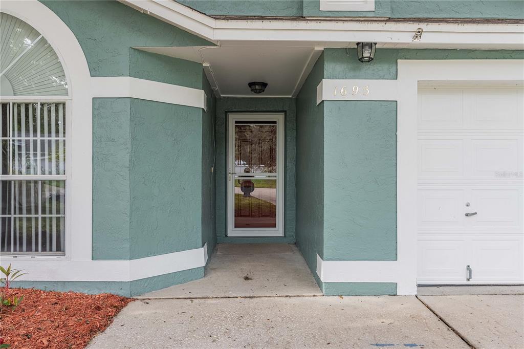 The exterior of a house features a teal stucco facade, a front door, and a garage — 1695 LAKESIDE DRIVE, BARTOW, FL