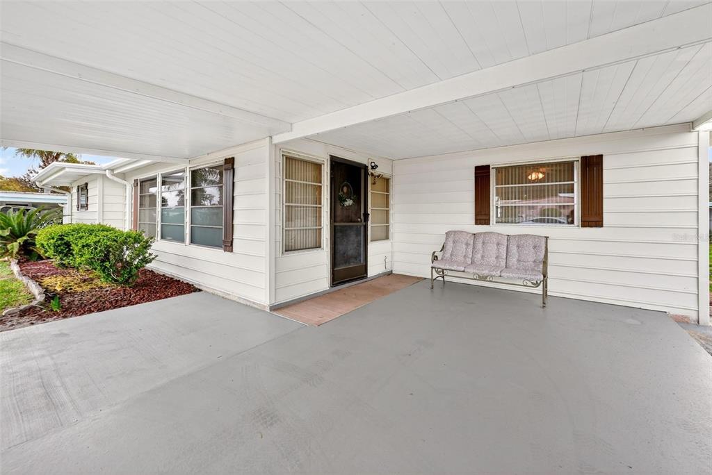 A covered concrete carport area features a front door, windows with shutters, and a bench — 11914 HICKORY LANE, TAVARES, FL