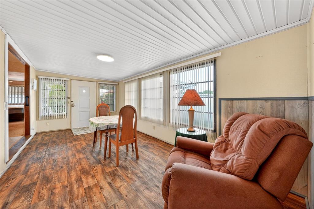 A sunroom features wood-look flooring, a dining set, a recliner, and vertical window blinds — 11914 HICKORY LANE, TAVARES, FL