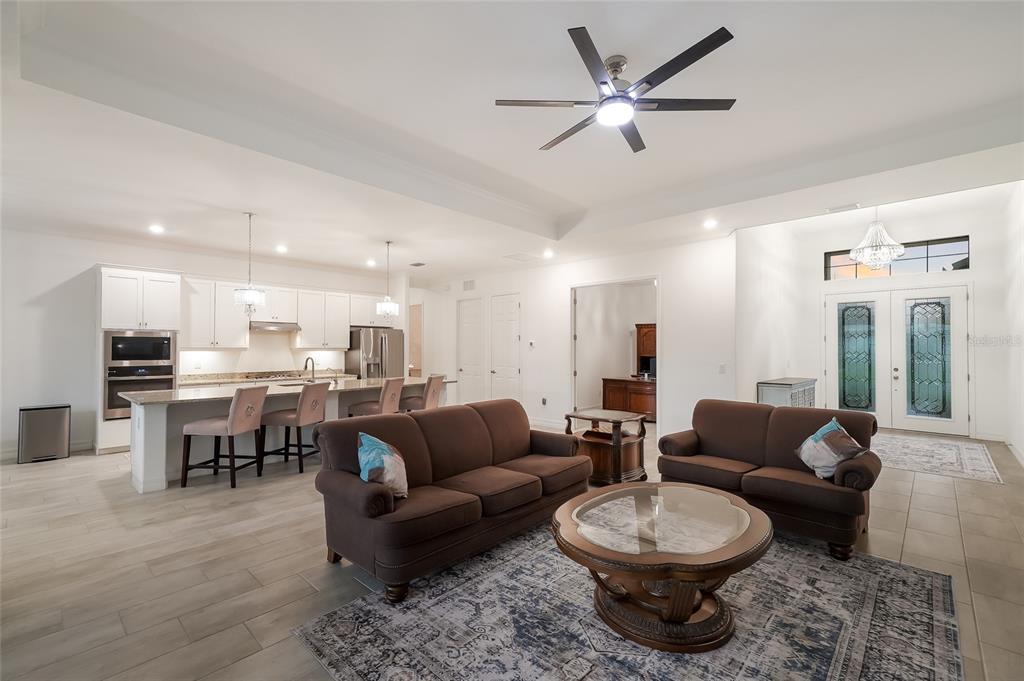 An open-concept living room and kitchen featuring tile floors, brown sofas, and a center island — 17528 POLO TRAIL, LAKEWOOD RANCH, FL