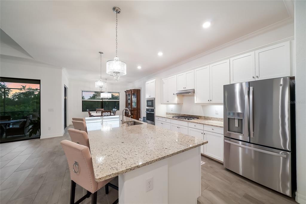 A modern kitchen features white cabinets, granite countertops, a large island, and stainless steel appliances — 17528 POLO TRAIL, LAKEWOOD RANCH, FL