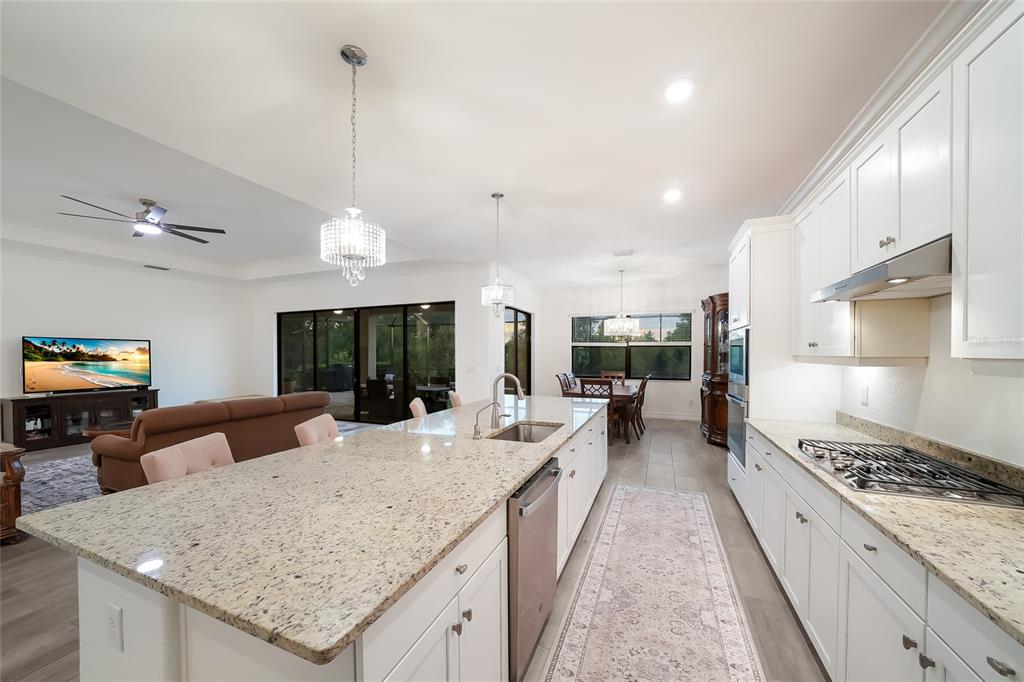 A bright kitchen with white cabinets, granite countertops, and a large island overlooks a living area — 17528 POLO TRAIL, LAKEWOOD RANCH, FL