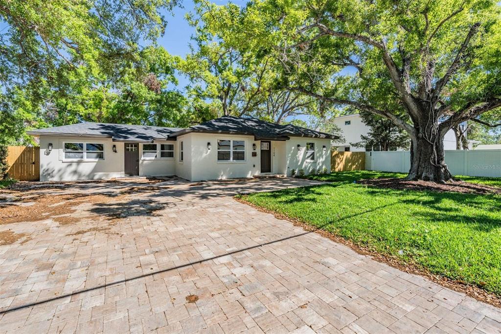 A single-story house with a paved driveway, white stucco exterior, and large shade trees — 1104 S LOIS AVENUE, TAMPA, FL