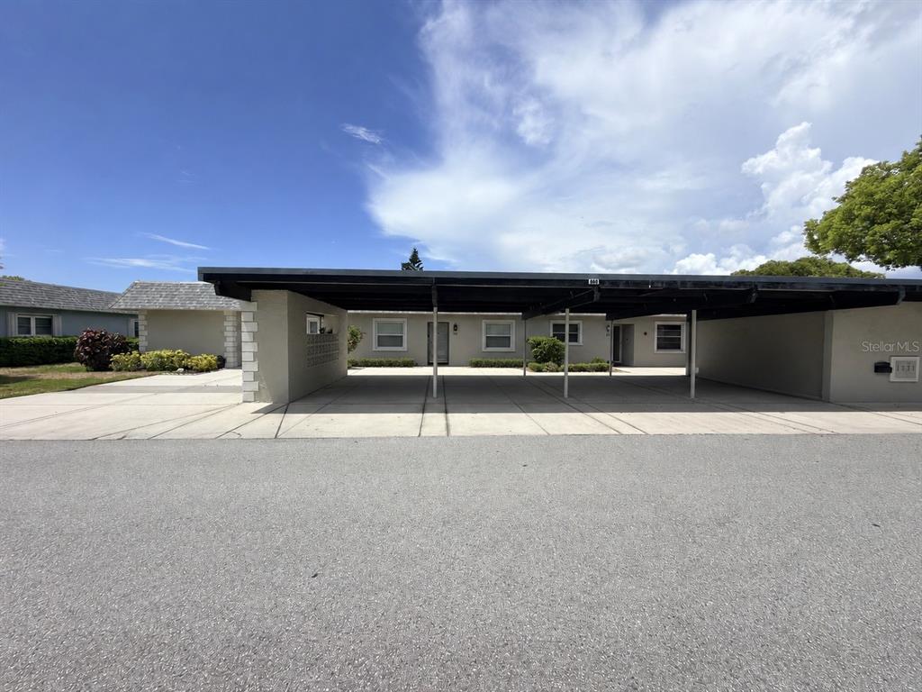 A single-story residential building features a large, flat-roofed carport covering a concrete driveway — 9703 GREENSKEEPER DRIVE, NEW PORT RICHEY, FL