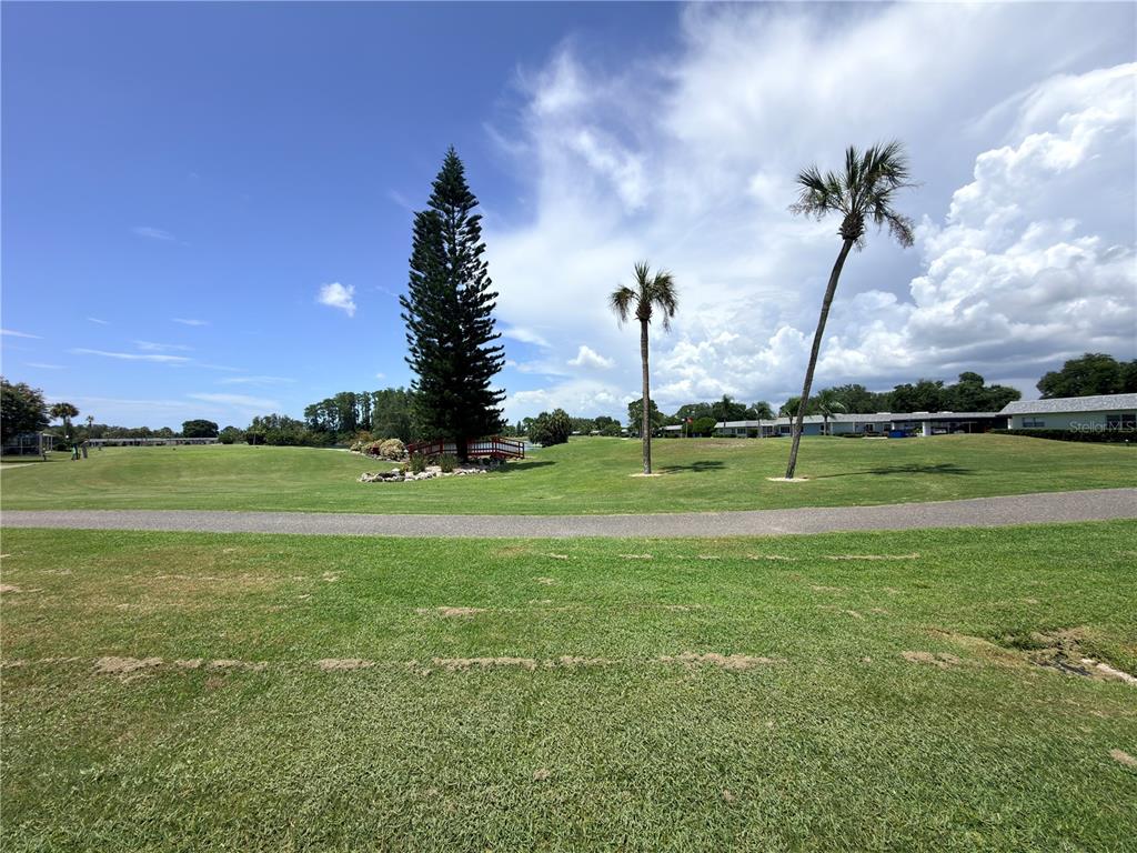 A paved path winds through a grassy golf course with a tall pine and palm trees — 9703 GREENSKEEPER DRIVE, NEW PORT RICHEY, FL