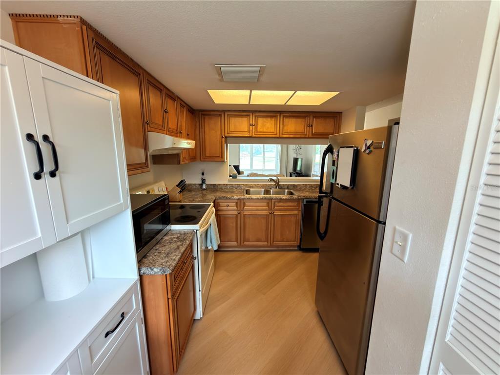 A kitchen features wood cabinets, stainless steel appliances, a pass-through window, and light-colored flooring — 9703 GREENSKEEPER DRIVE, NEW PORT RICHEY, FL