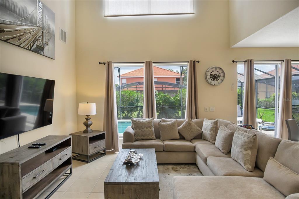 A living room features a sectional sofa, a television, and a balcony overlooking the space — 134 SEVILLA AVENUE, DAVENPORT, FL