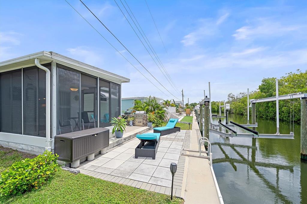 A patio with lounge chairs sits beside a canal with boat lifts and a screened porch — 192 BIMINI DRIVE, PALMETTO, FL