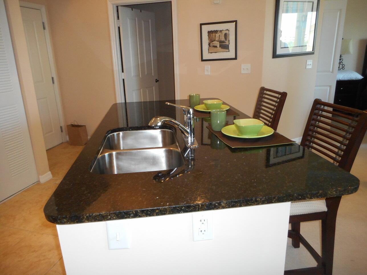 A kitchen island with a double sink, dark granite countertops, and two place settings — 600 S Dixie Highway # 452, West Palm Beach FL 33401, WEST PALM BEACH, FL