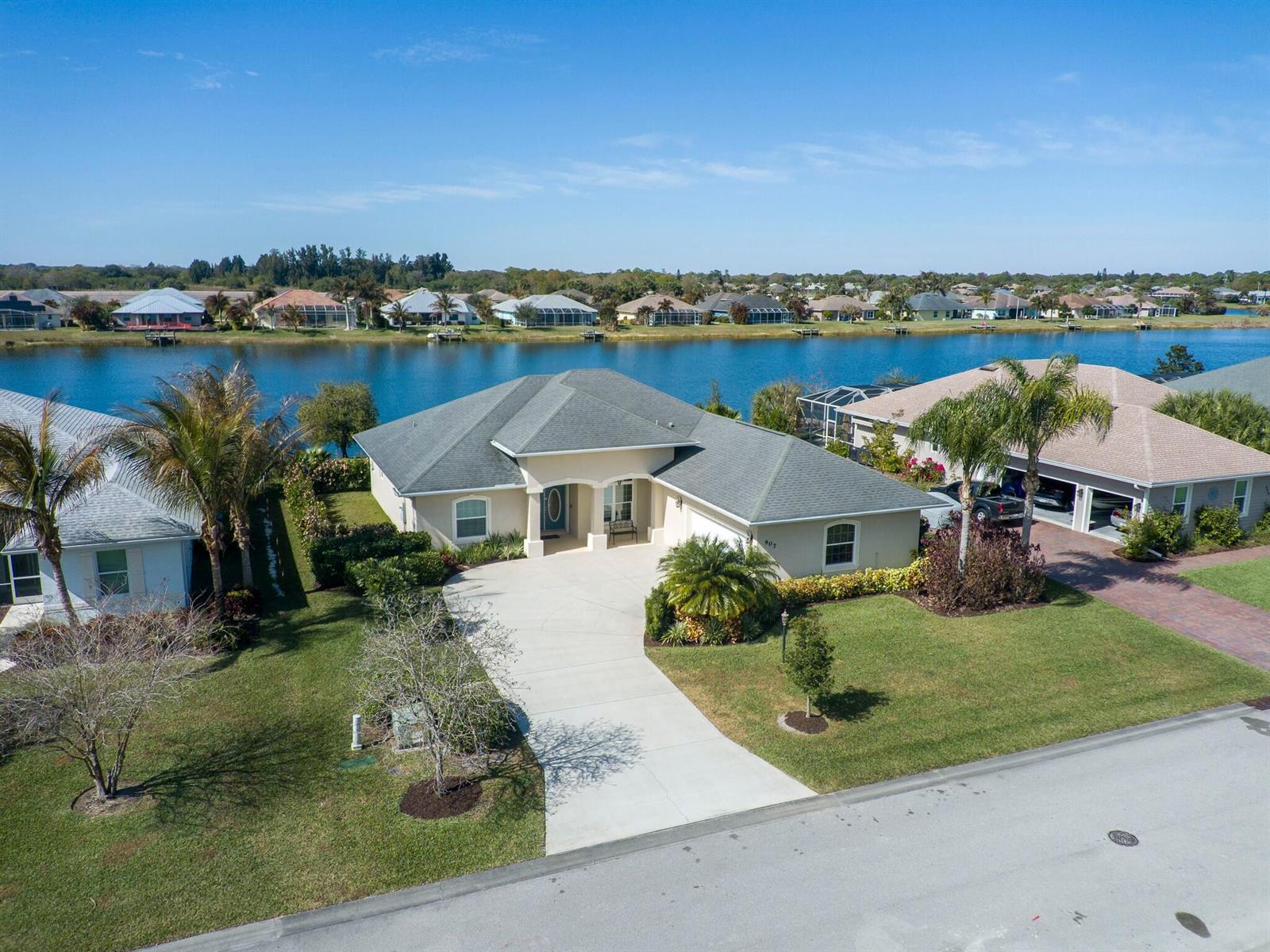 An aerial view shows a single-story house with a concrete driveway and a backyard lake — 907 Yearling Trail, Sebastian FL 32958, SEBASTIAN, FL