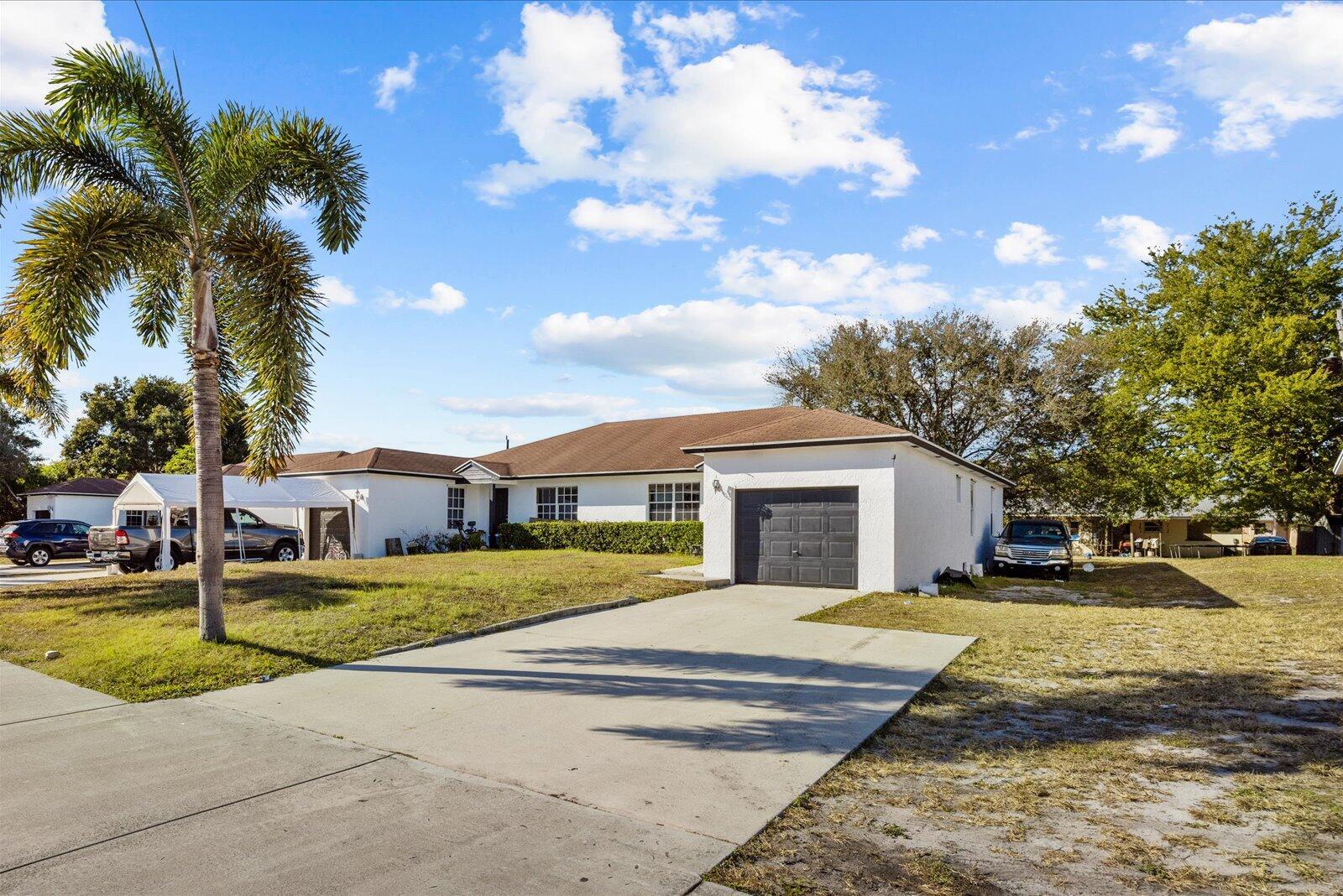 A white single-story house with a brown roof, a garage, and a palm tree — 2593 SE Indian Street, Stuart FL 34997, STUART, FL