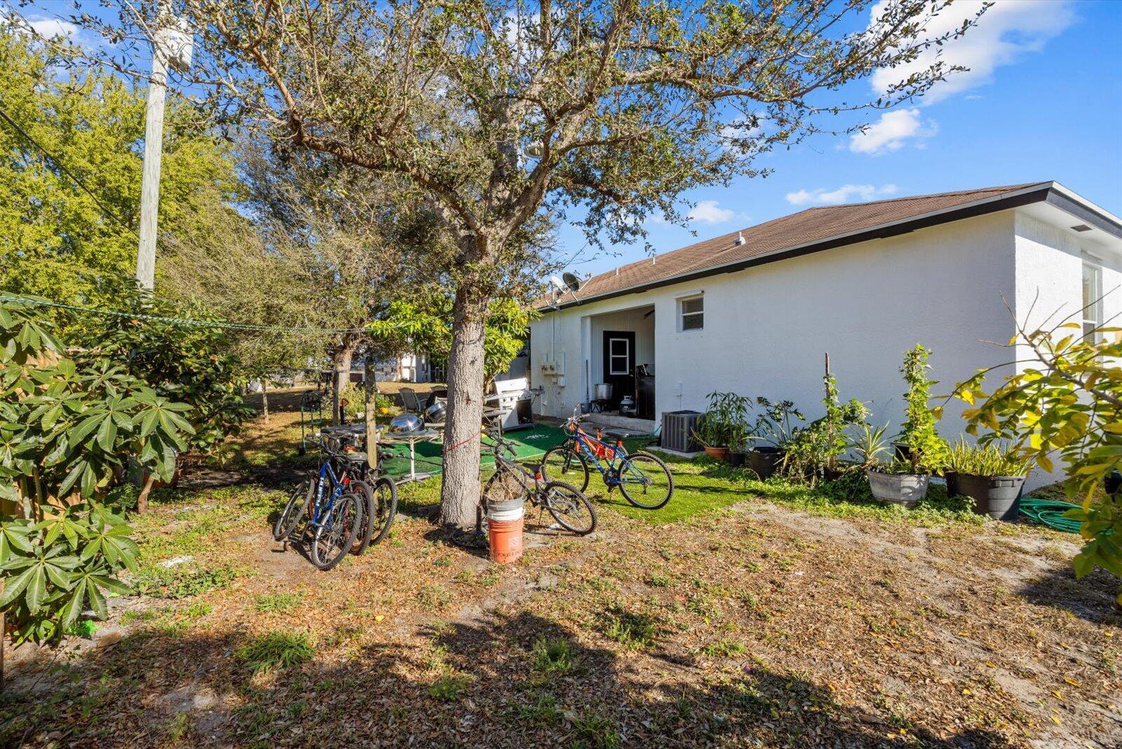 A backyard view shows a white house exterior, a large tree, and several parked bicycles — 2593 SE Indian Street, Stuart FL 34997, STUART, FL