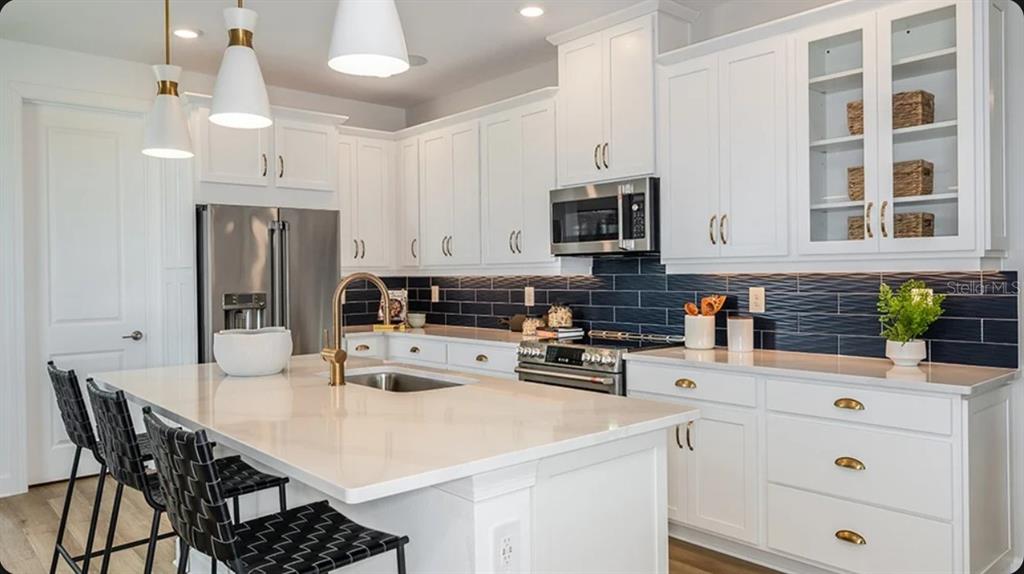 A modern kitchen features white cabinets, a large island with gold fixtures, and dark tile backsplash — 4463 OCHOS RIOS PLACE, KISSIMMEE, FL