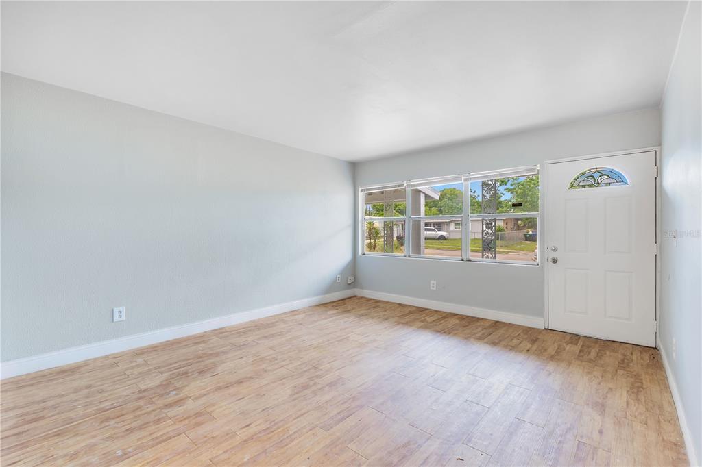 An empty living room features light gray walls, wood-look tile flooring, and a white front door — 6132 W LIVINGSTON STREET, ORLANDO, FL
