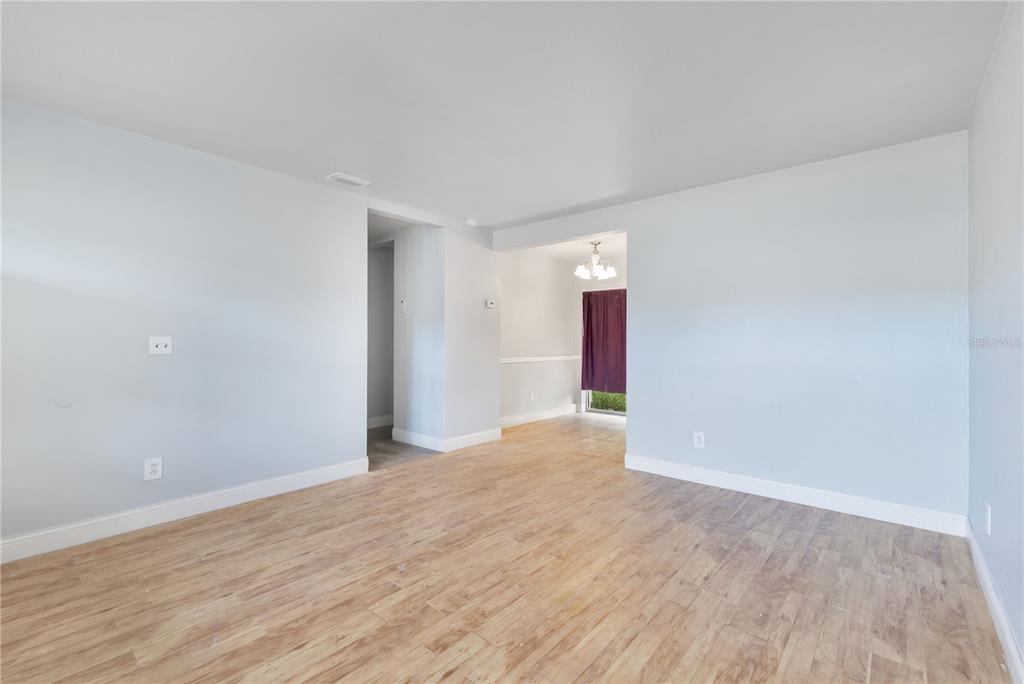 An empty room with light gray walls, wood-look flooring, and an adjacent dining area — 6132 W LIVINGSTON STREET, ORLANDO, FL