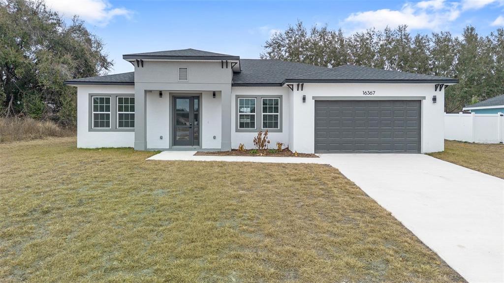 A single-story house with white stucco walls, a gray garage, and a dark shingled roof — 16367 SW 16TH COURT, OCALA, FL