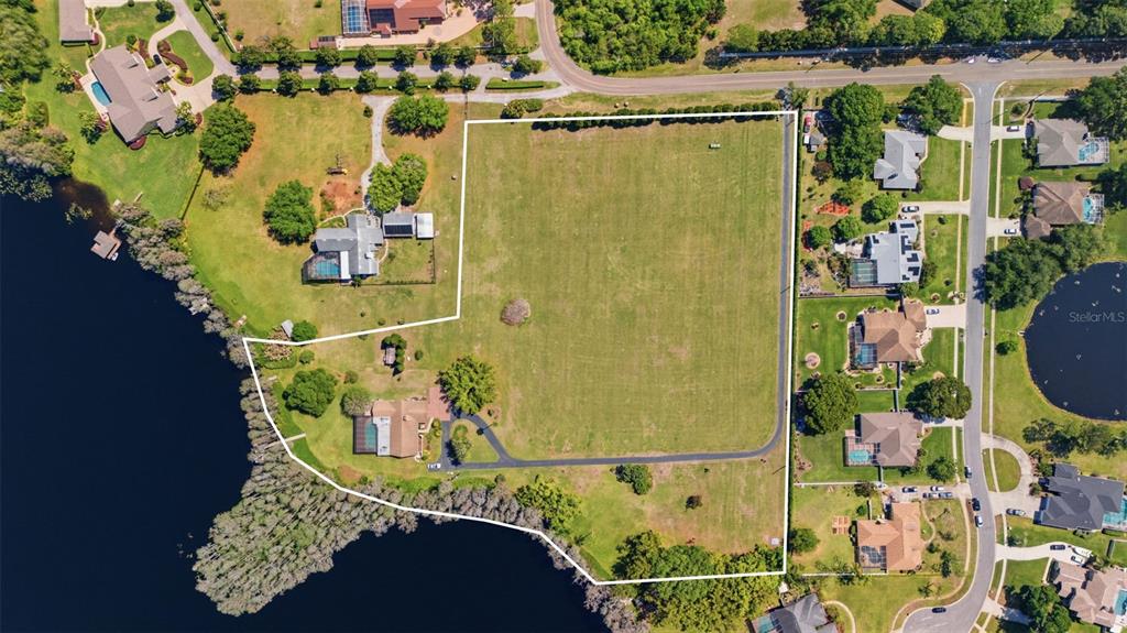 An aerial view shows a large, grassy vacant lot bordered by residential homes and a lake — 820 NEWBERGER ROAD, LUTZ, FL