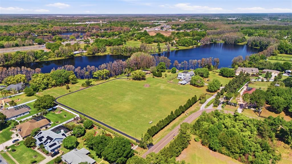 An aerial view shows a large, grassy lot bordered by a road and a lake — 820 NEWBERGER ROAD, LUTZ, FL