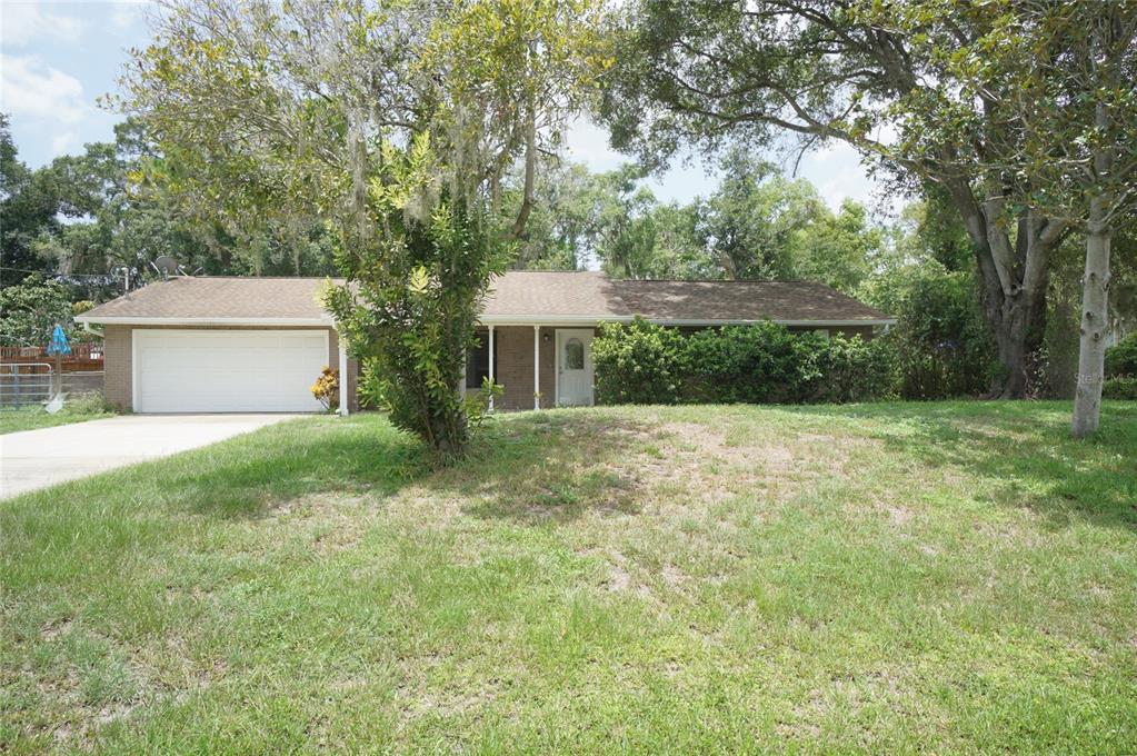 A single-story brick house with a two-car garage sits on a grassy, tree-shaded lot — 6005 CHRISTY LANE, RIVERVIEW, FL