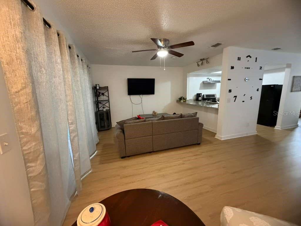 A living room with light wood-look flooring, a gray sectional sofa, and a wall-mounted television — 2437 SUMMERFIELD WAY, KISSIMMEE, FL