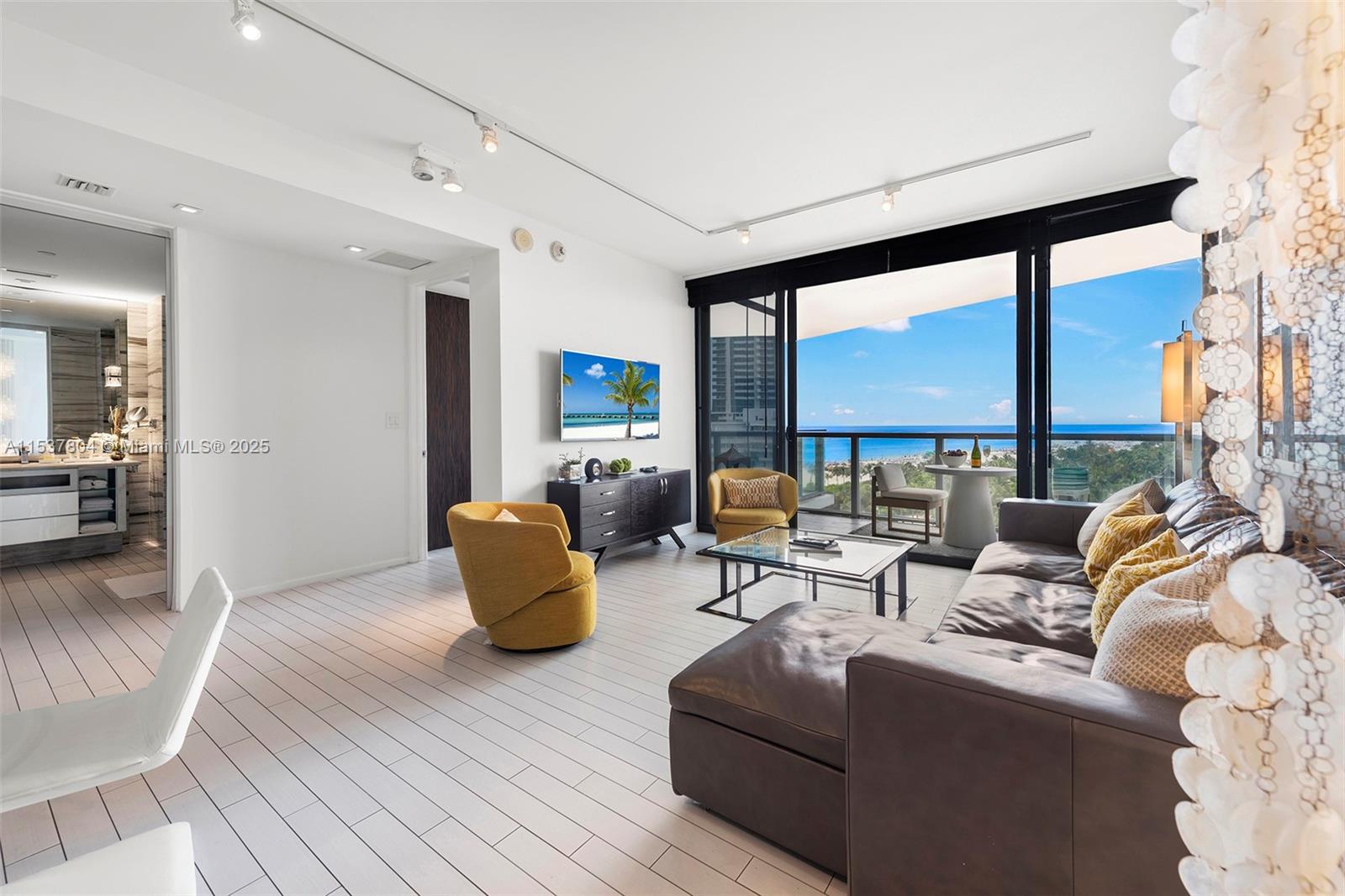 A modern living room features a dark leather sectional, yellow armchairs, and a balcony view — 2201 Collins Ave # 814, Miami Beach FL 33139, MIAMI BEACH, FL