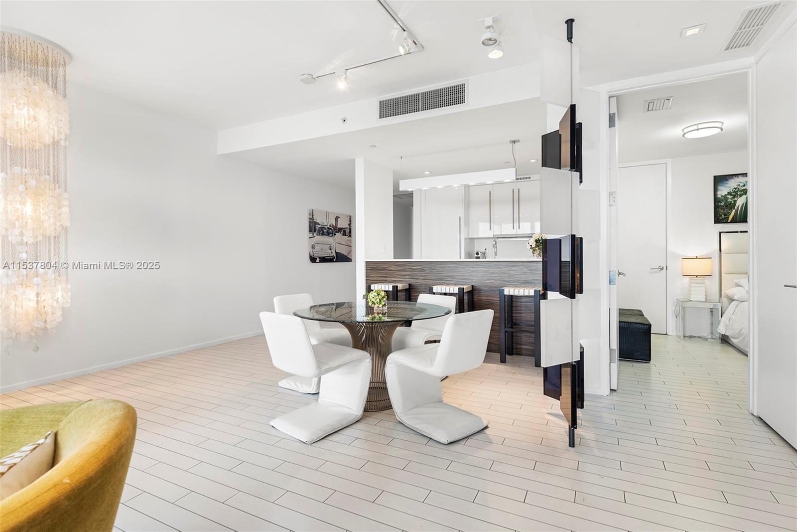 A dining area with a glass table and white chairs sits before a kitchen counter — 2201 Collins Ave # 814, Miami Beach FL 33139, MIAMI BEACH, FL